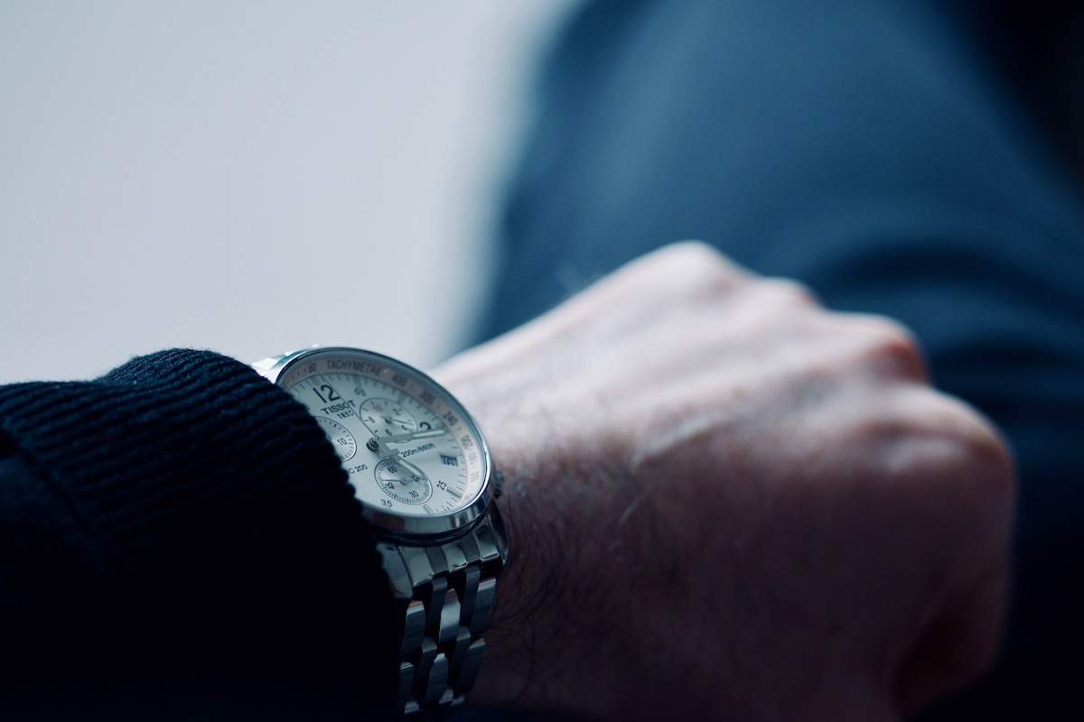 Photo of hand and Tissot wrist watch with focus on the time in cold blue colours ageing us