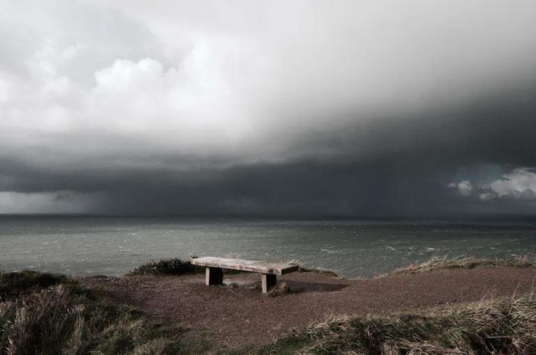 Wooden bench overlooking the sea beneath dark storm clouds

